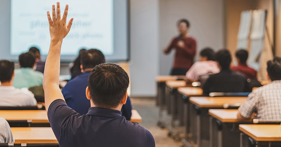 Man with his back to the camera raising his hand in a classroom
