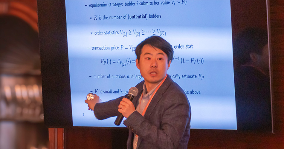 Man standing in front of screen with equations on it holding a microphone
