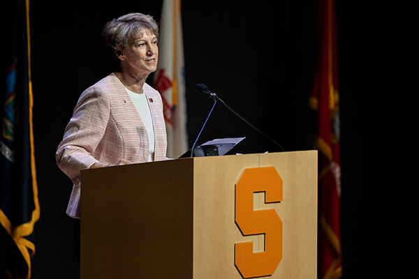 Person speaking at a podium with the Syracuse University logo on it.