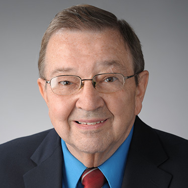 Professional headshot of an individual smiling, wearing glasses, a navy blue suit, and a red tie.