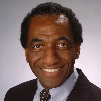 Person with dark hair wearing a suit and tie.